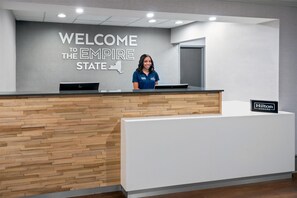 A reception desk with a 'WELCOME TO THE EMPIRE STATE' sign, a laptop, and a 'Hilton Honors' sign. - Hampton Inn Buffalo-Airport / Galleria Mall (Buffalo)
