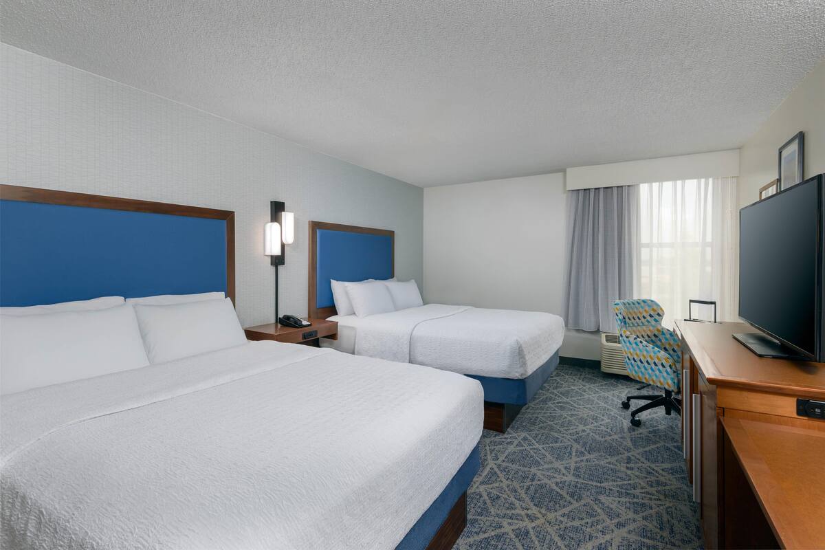 Une chambre d’hôtel avec deux lits, un bureau avec une télévision et une chaise.