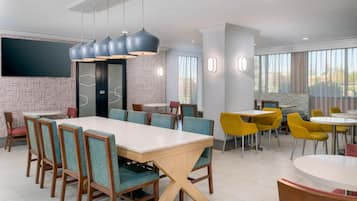 A modern dining area with a long table, multiple chairs, and a television mounted on the wall.