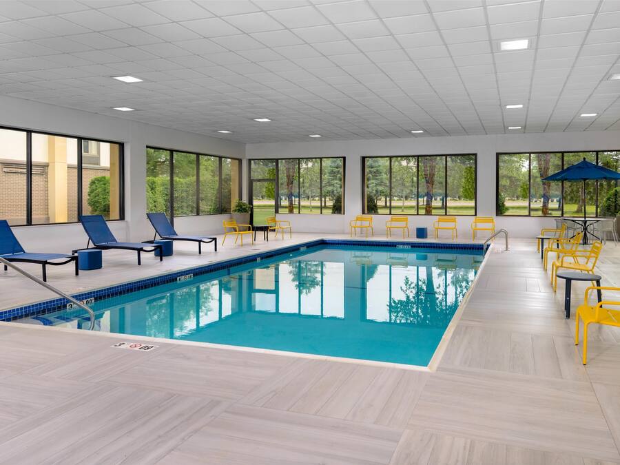 Une piscine intérieure dotée de chaises longues bleues et jaunes, de grandes fenêtres et d’un sol carrelé.