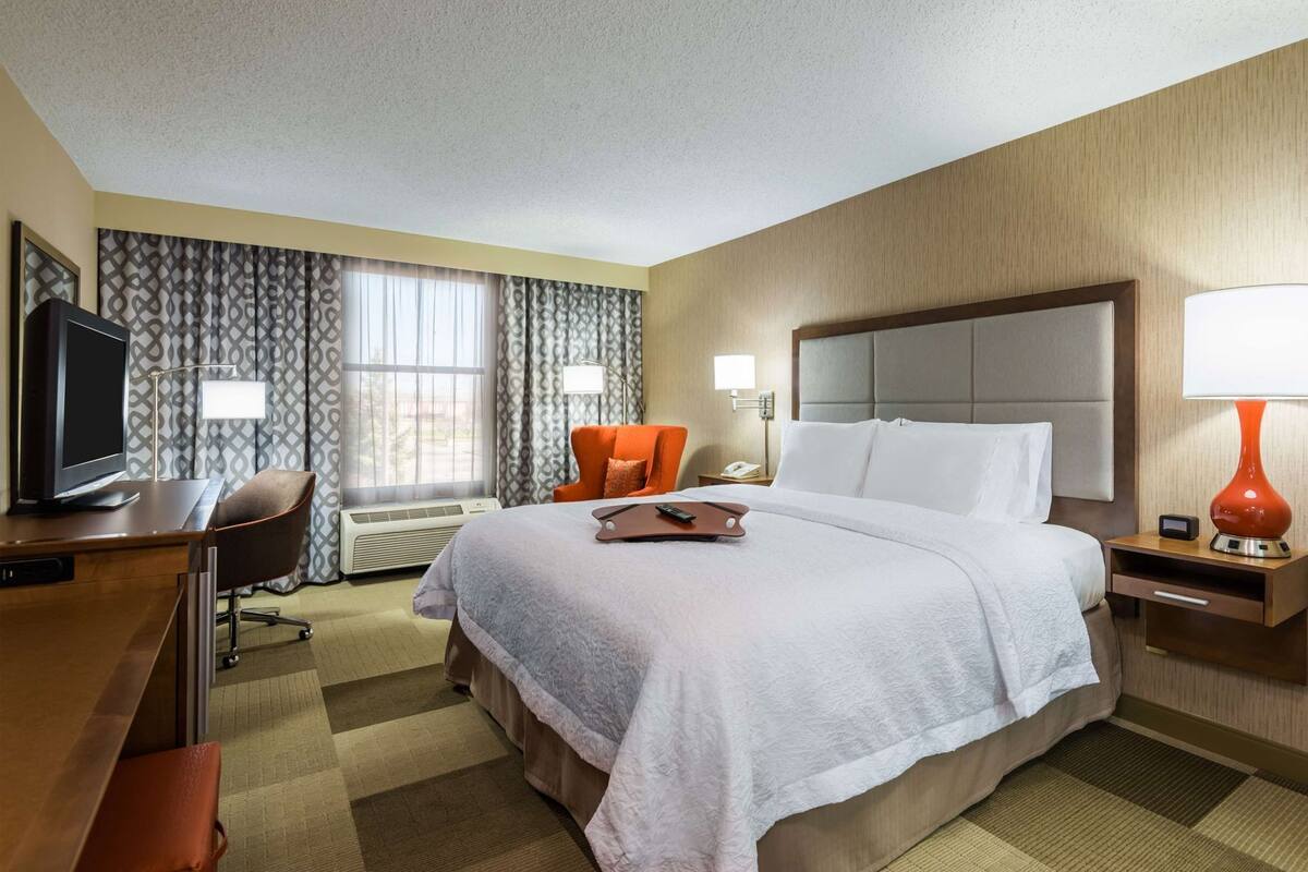 Une chambre d’hôtel équipée d’un lit, d’un bureau, d’une chaise, d’une télévision et d’une fenêtre avec des rideaux.