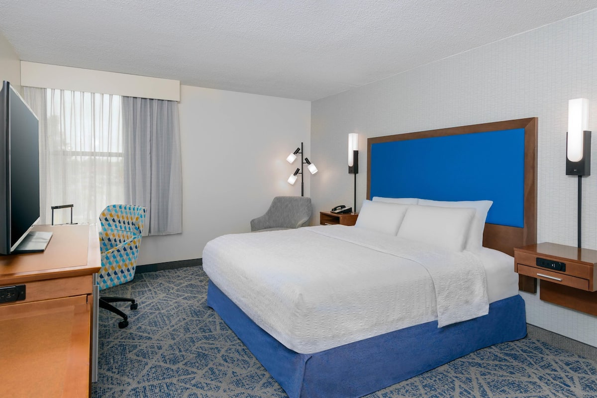 Une chambre d’hôtel avec un grand lit, un bureau avec un ordinateur, une chaise et une télévision.