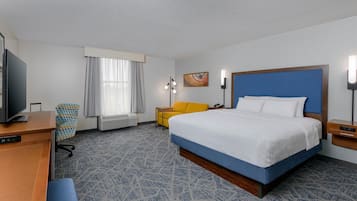 A hotel room with a large bed, a desk with a computer, a chair, a television, and a window with curtains.