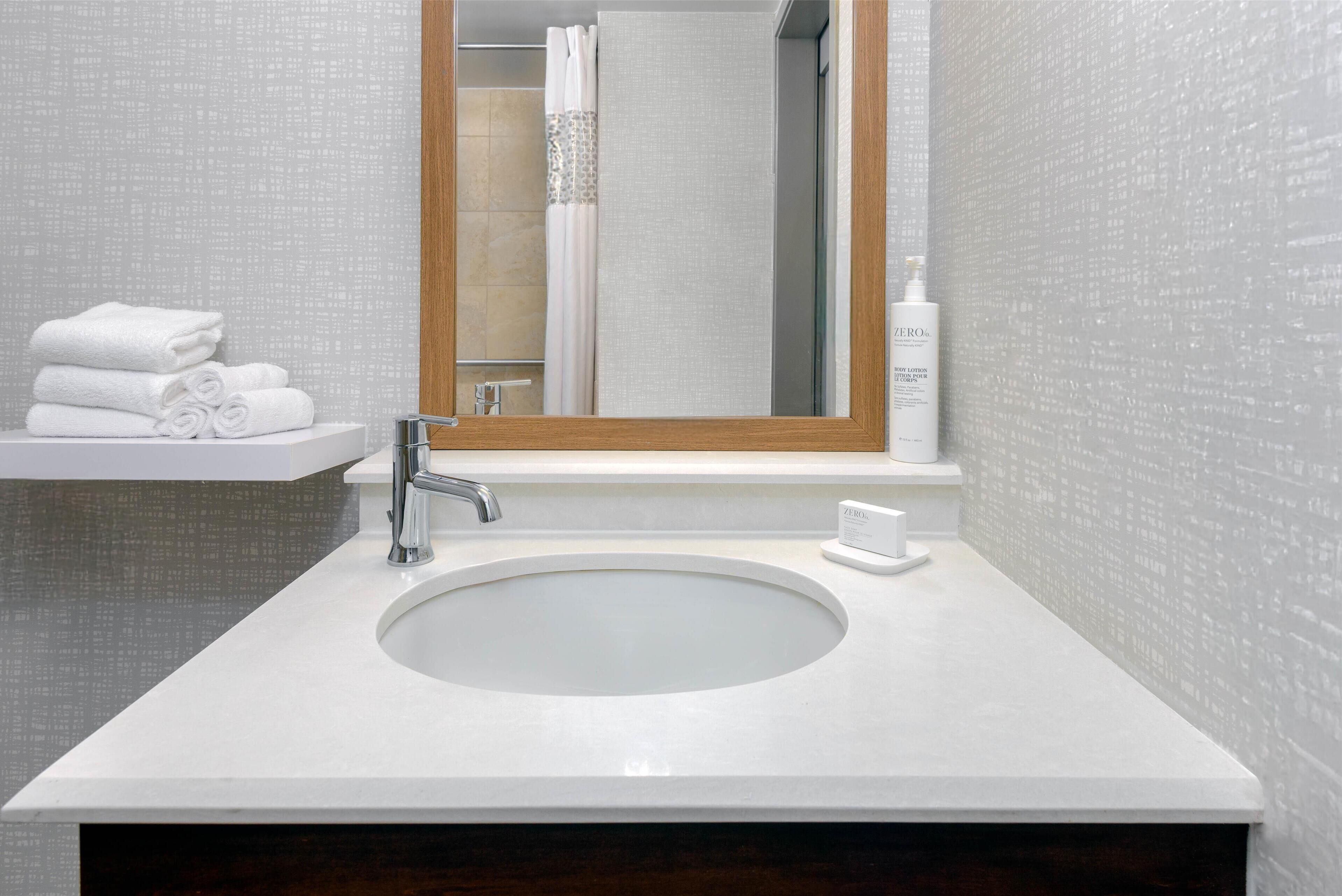 A bathroom with a white sink, a mirror, and a towel stack.