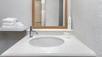 A bathroom with a white sink, a mirror, and a towel stack.