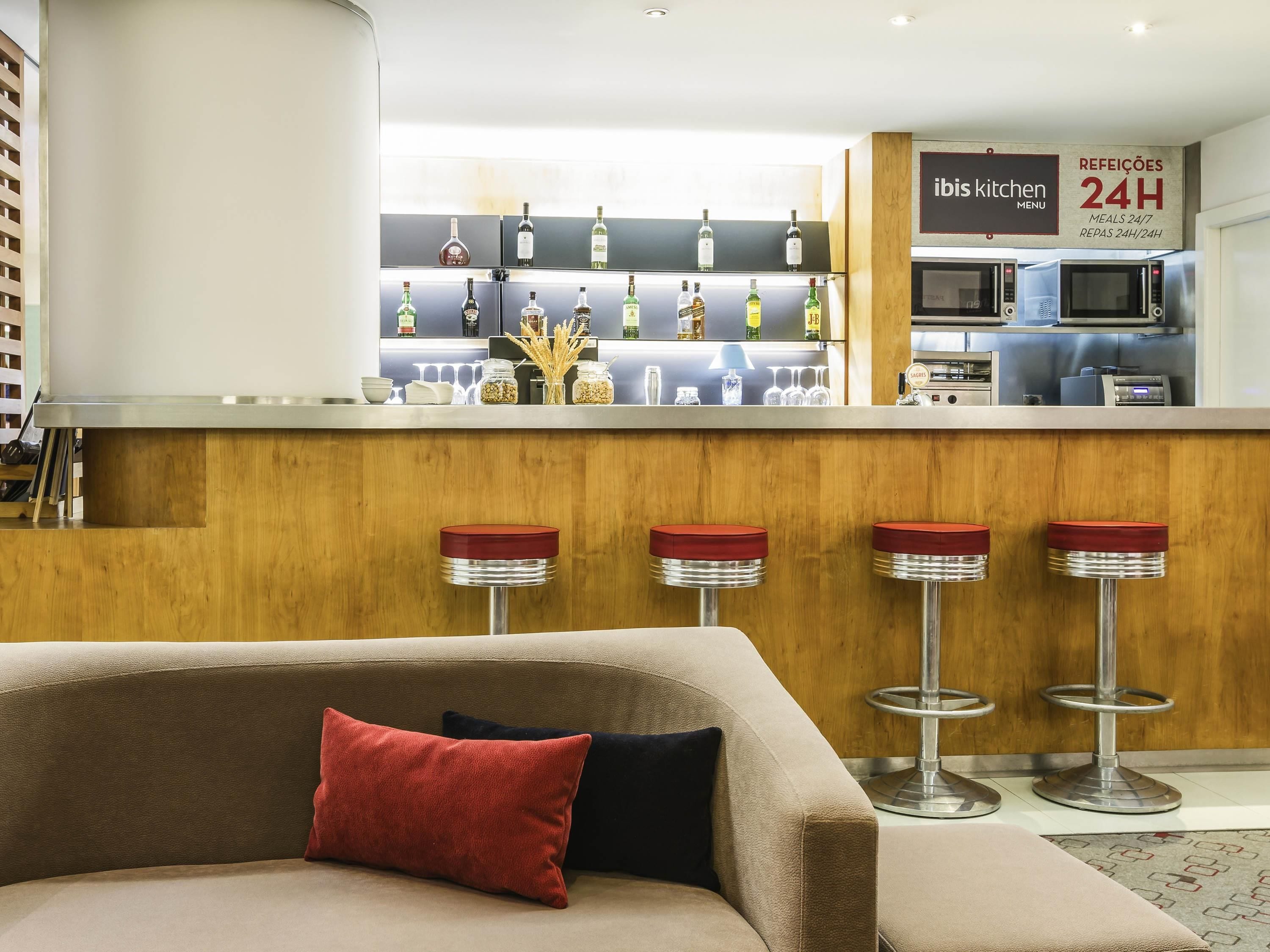 A modern bar area with a minibar, stools, and a sign indicating 24-hour meal service.