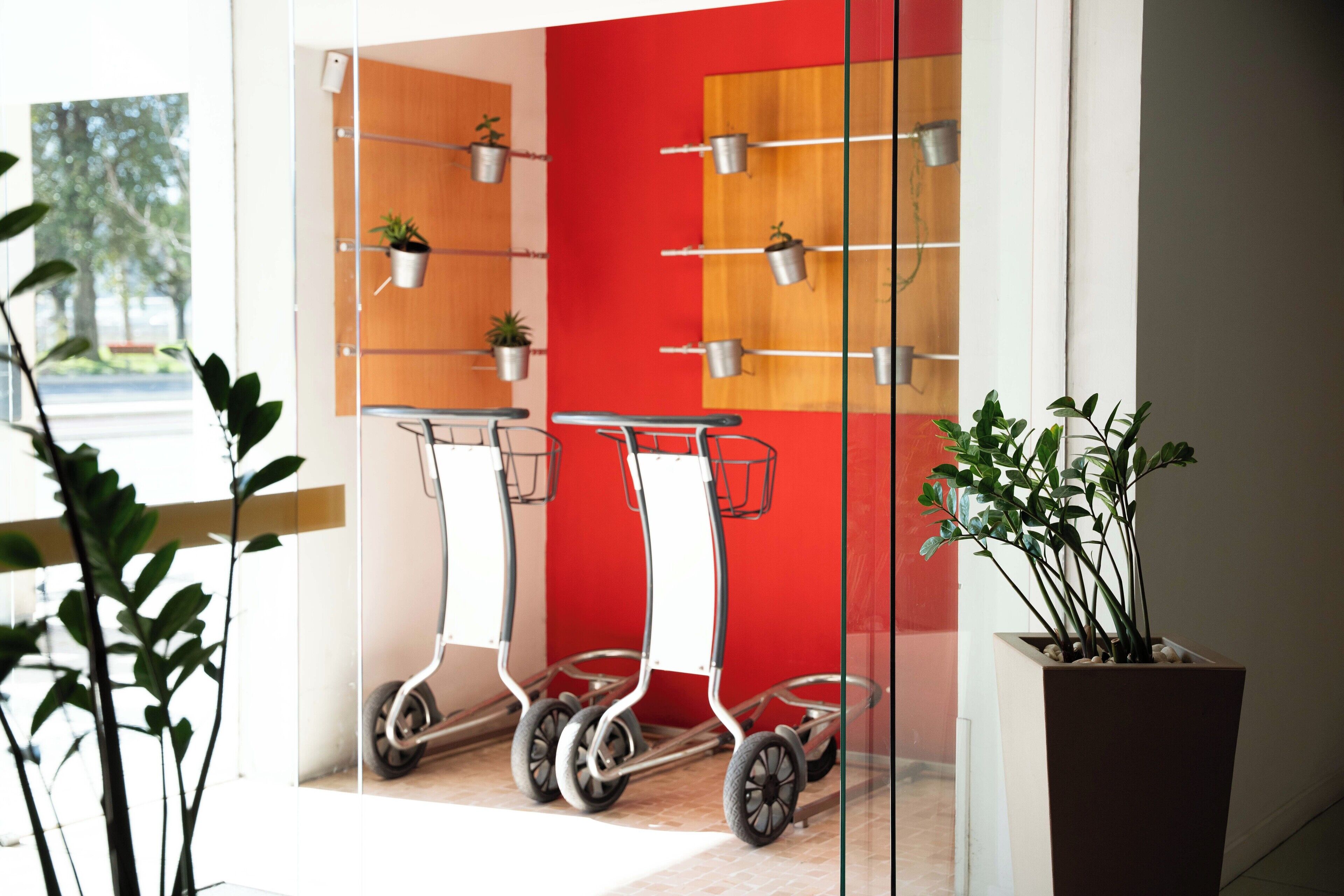 Ein modernes Interieur mit einer roten Wand, zwei Rollwagen und Topfpflanzen.