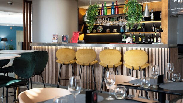 A bar area with a counter, bar stools, and a variety of bottles and glasses. - ibis Coimbra Centro (Coimbra)