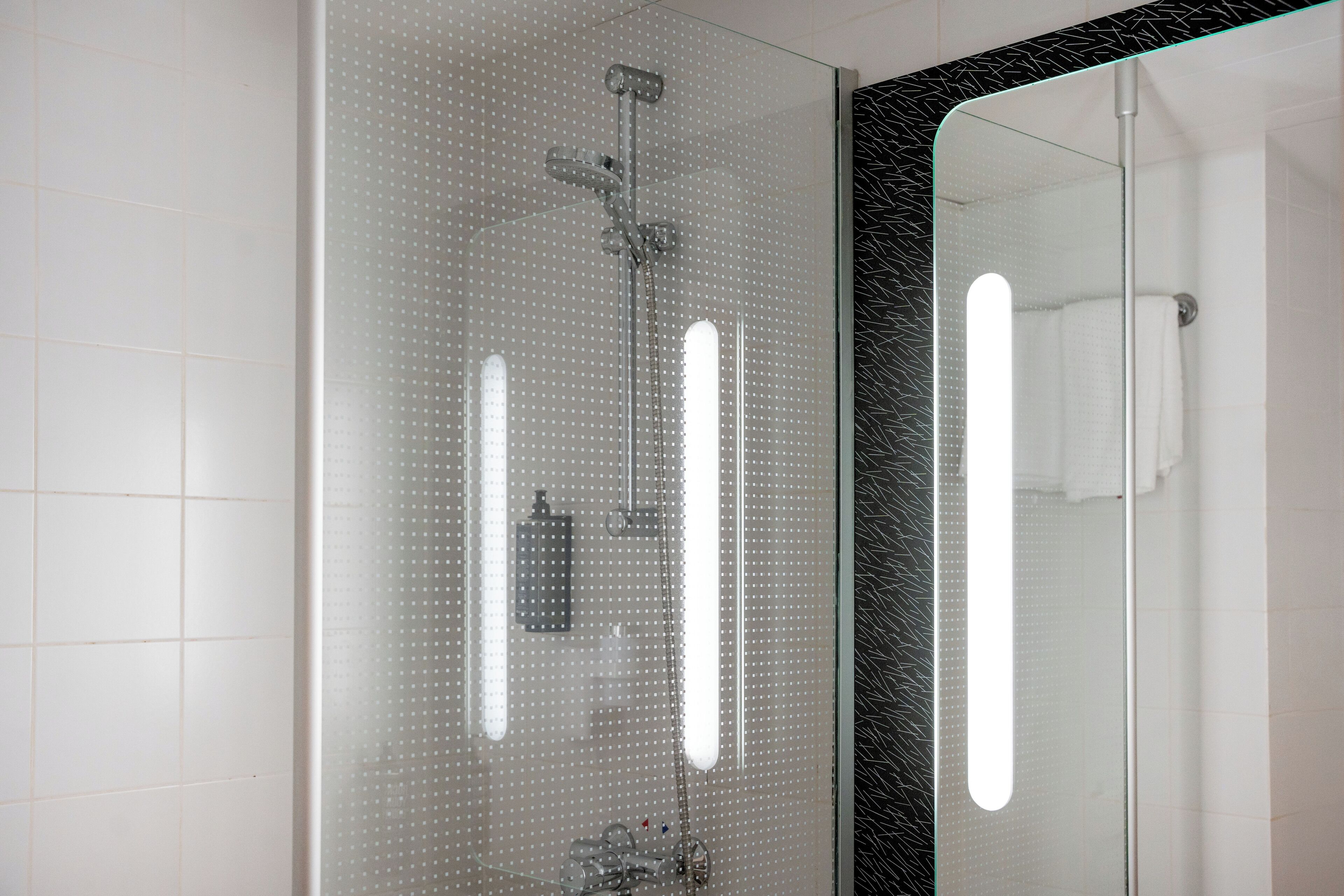 A modern bathroom with a glass shower enclosure, a large mirror, and a black marble countertop.