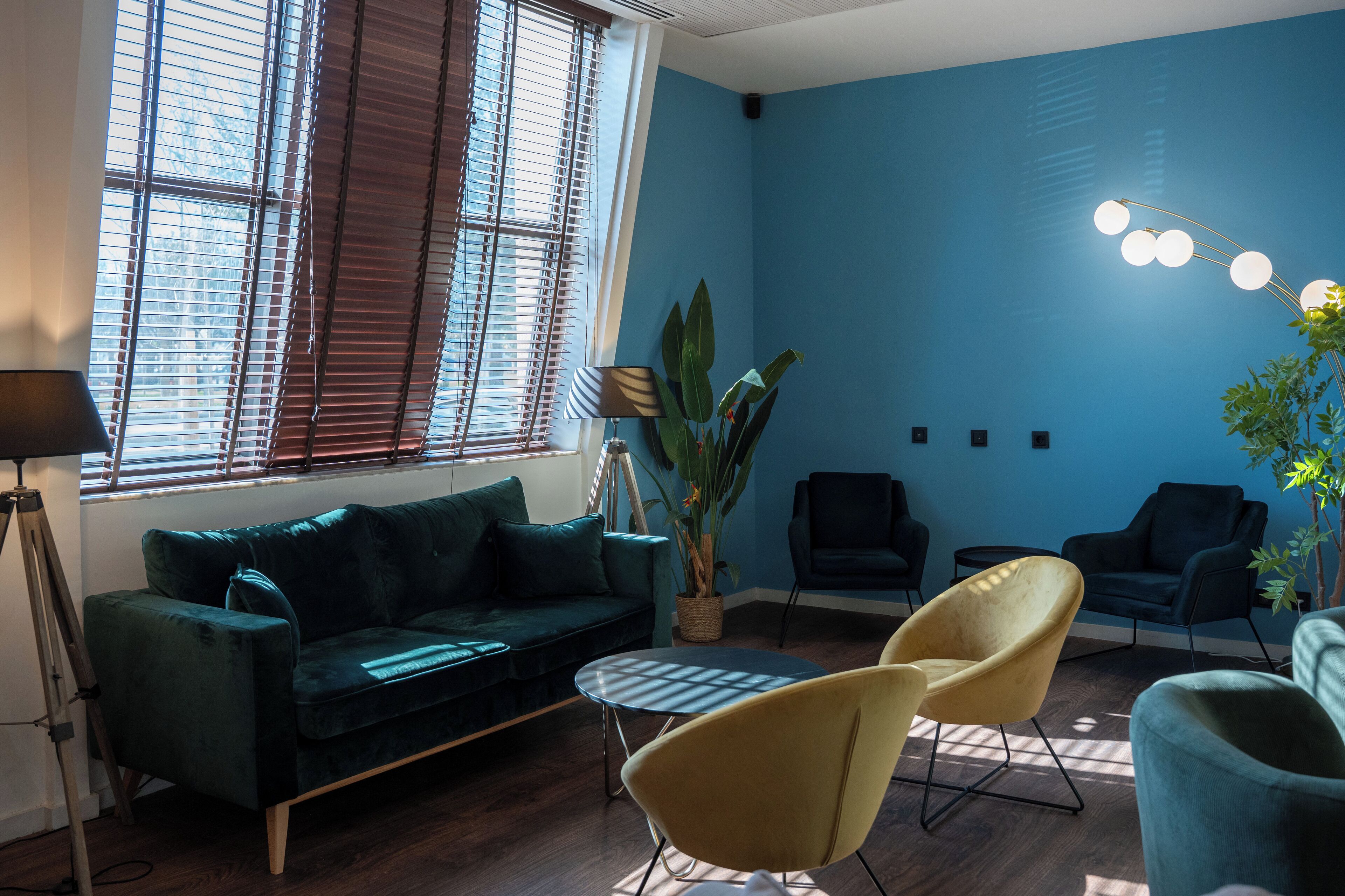 A modern living room with a dark green sofa, two yellow chairs, and a blue wall.