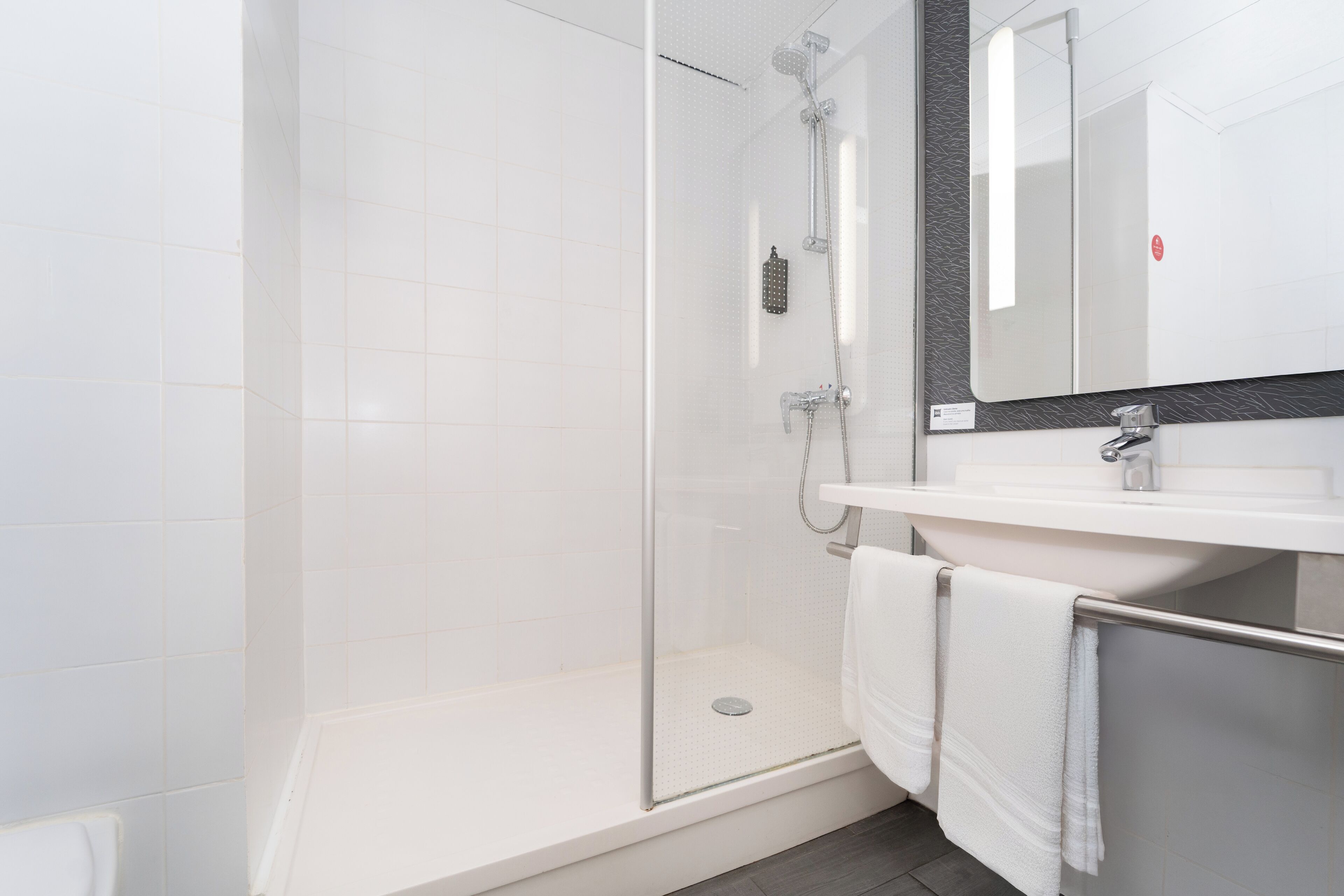 A modern bathroom with a glass-enclosed shower, a white sink, and a large mirror.