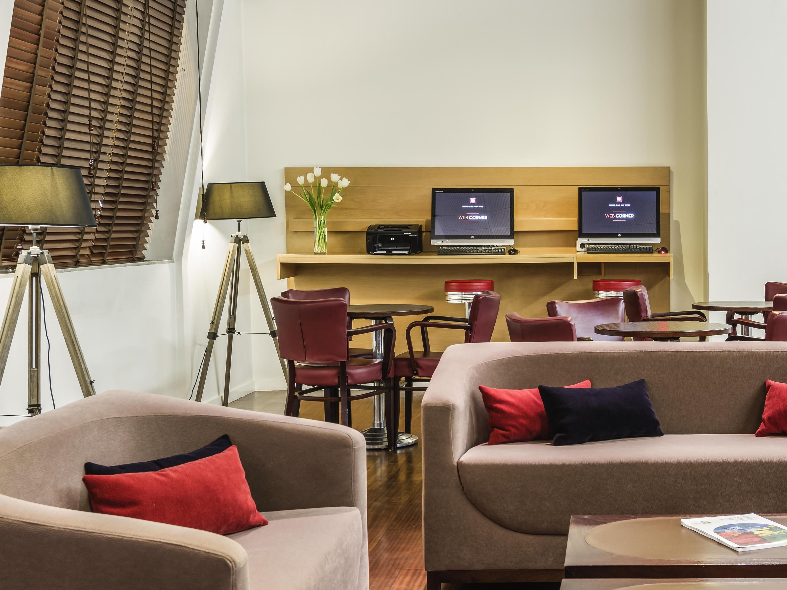 A hotel lobby with sofas, chairs, a desk with computers, and a lamp.