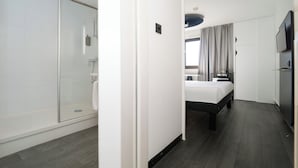Hotellihuone, jossa on suihku, sänky, televisio ja ikkuna, jossa on verhot.