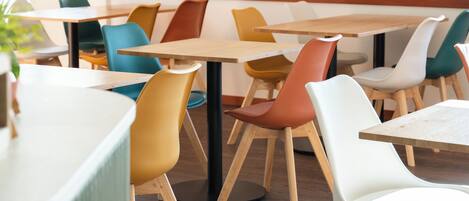 A dining area with wooden tables and colorful chairs, a wall-mounted light fixture, and two framed pictures.