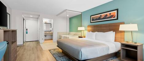 Una habitación de hotel con cama, mesitas de noche, televisor, baño y un pasillo.