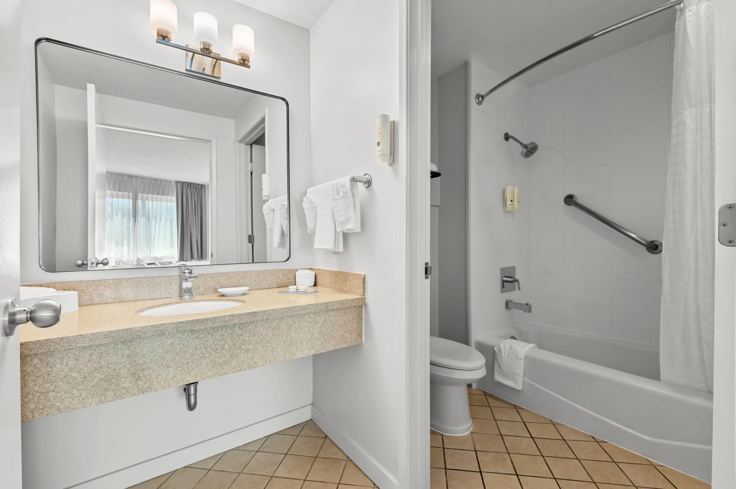 A bathroom with a sink, mirror, towel rack, toilet, and a shower area.