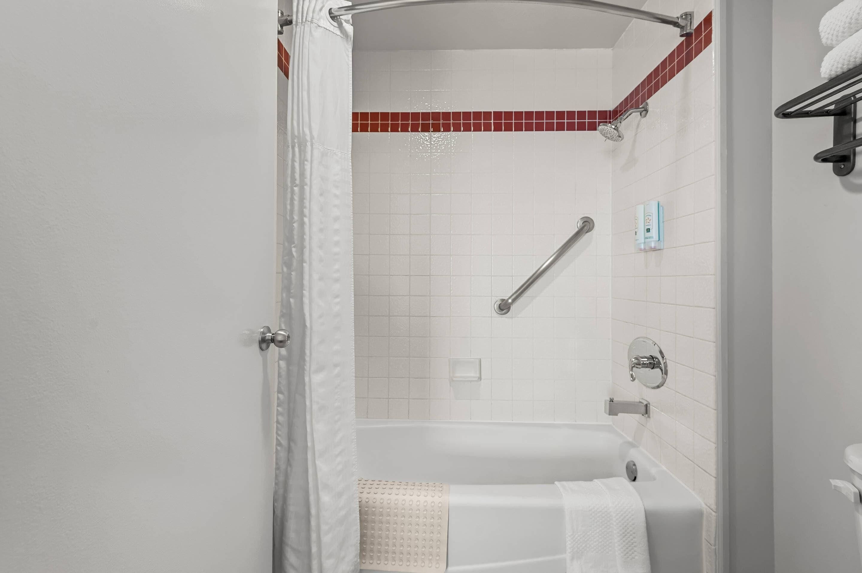 A bathroom with a bathtub, shower, and handrails.
