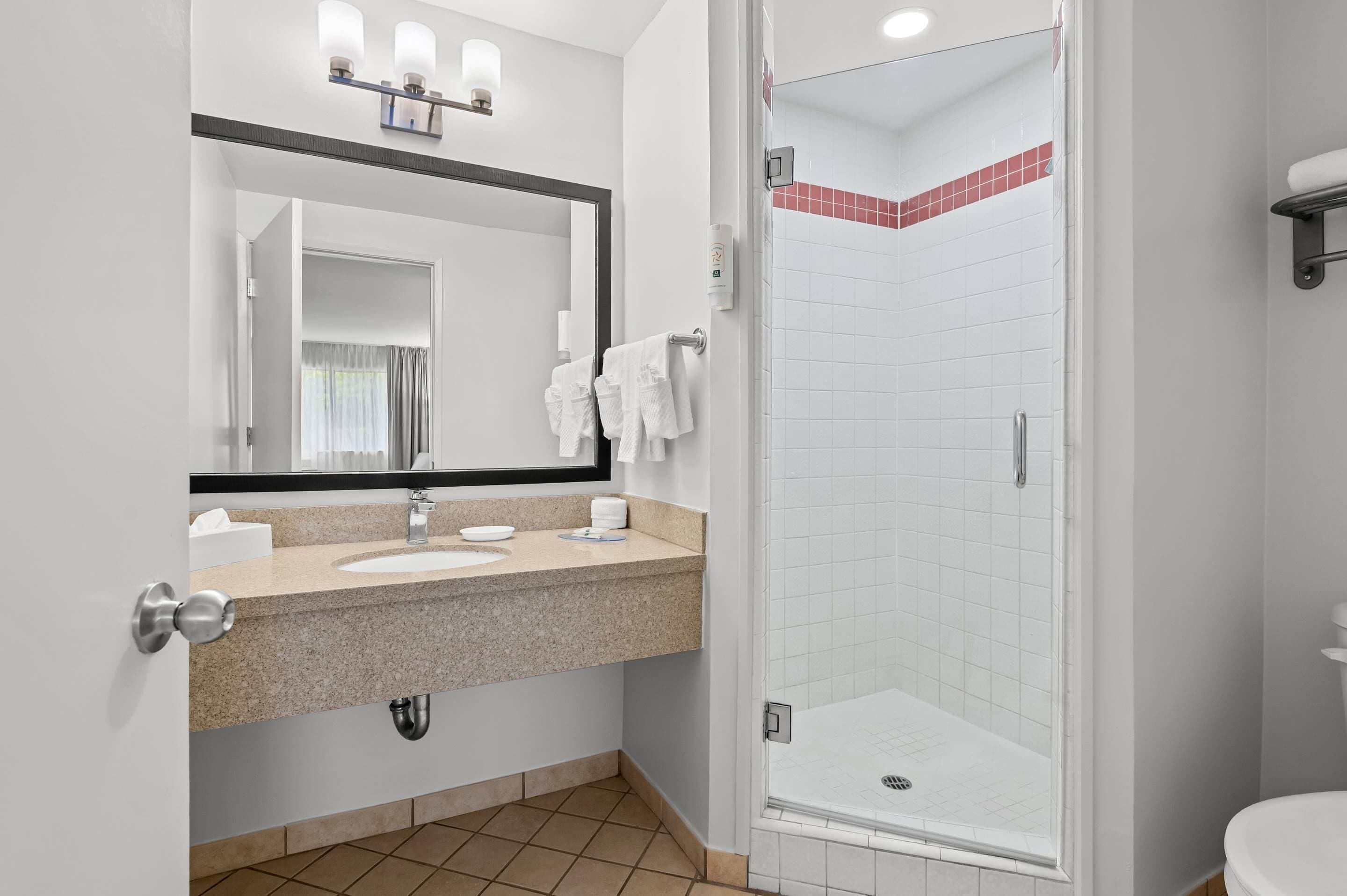 A bathroom with a sink, mirror, towel rack, and a shower area.