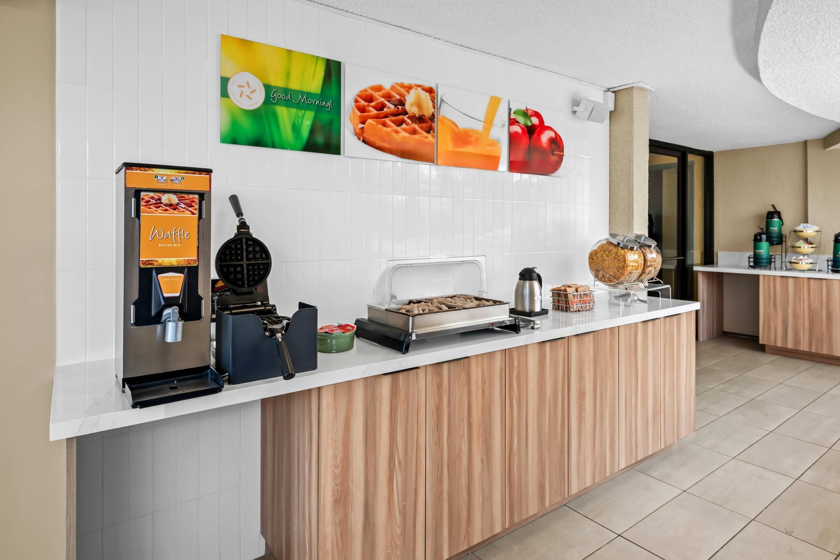 Ein Frühstücksbuffet mit Waffel- und Kaffeemaschinen, einer Waffeleisen und einer Obstauslage.
