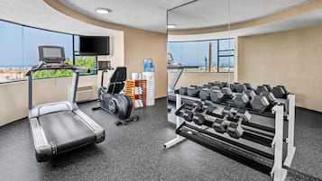 A gym with a treadmill, dumbbells, and a TV screen.
