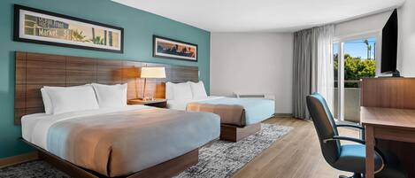 A hotel room with two beds, a desk, a chair, a TV, and a window with curtains.