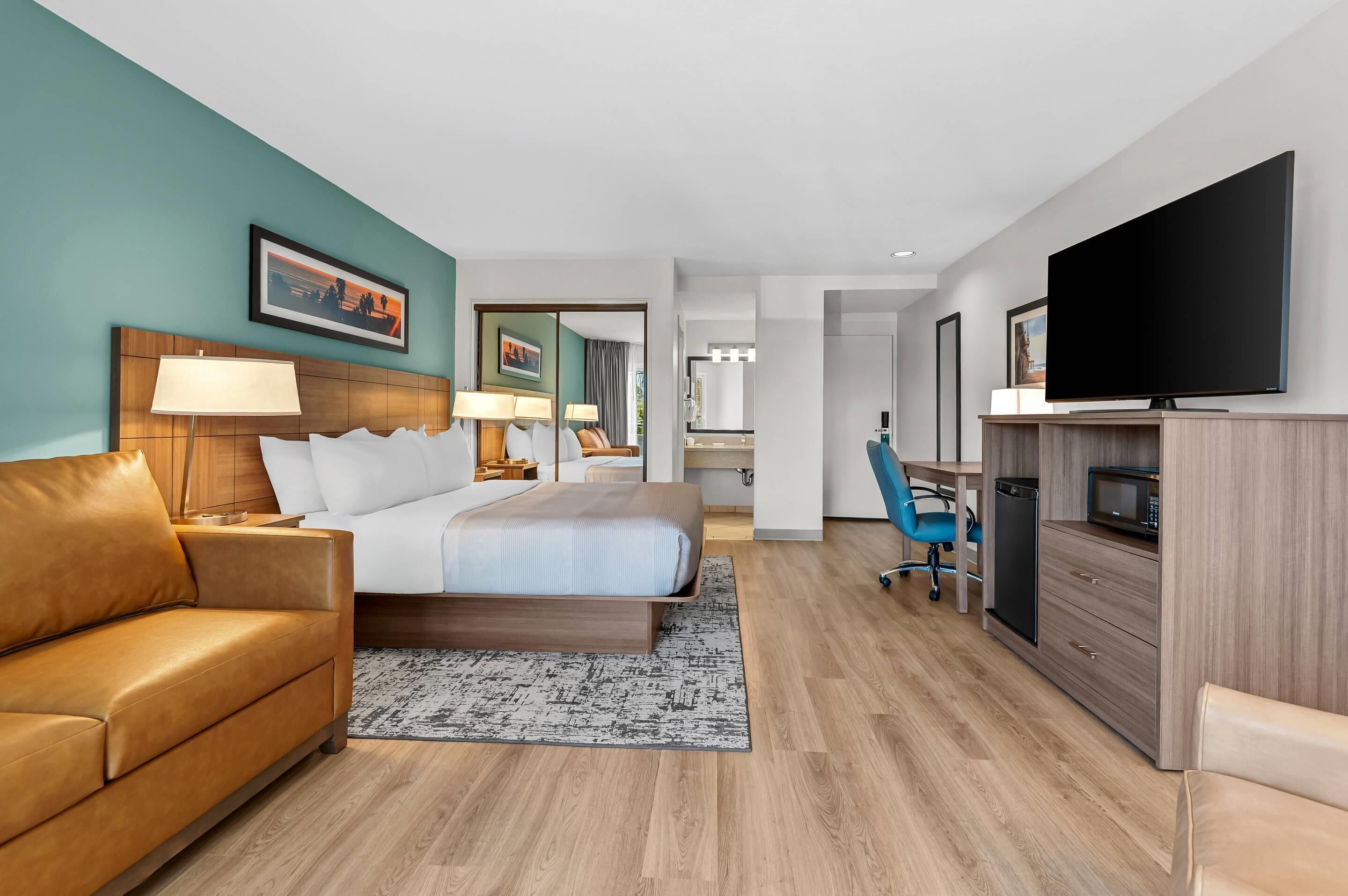 Ein modernes Hotelzimmer mit Bett, Sofa, Schreibtisch, Fernseher und Mikrowelle.