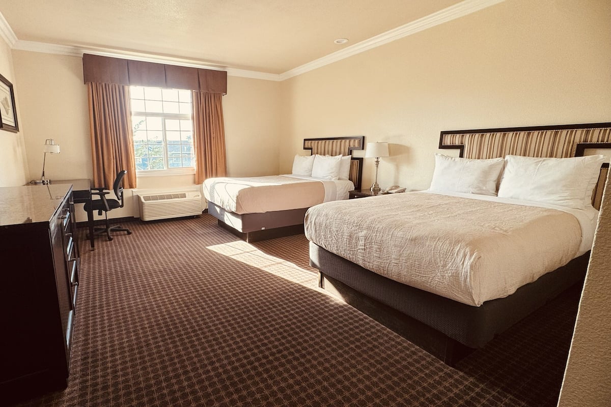A hotel room with a large bed, a smaller bed, a desk with a chair, a television, and a window with curtains.