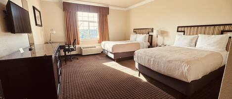 A hotel room with a large bed, a smaller bed, a desk with a chair, a television, and a window with curtains.