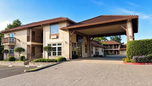 Een hotel met een overdekte ingang, een aangelegde oprijlaan en een heldere lucht.