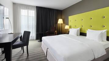 A hotel room with a large bed, a desk, a chair, and a lamp.