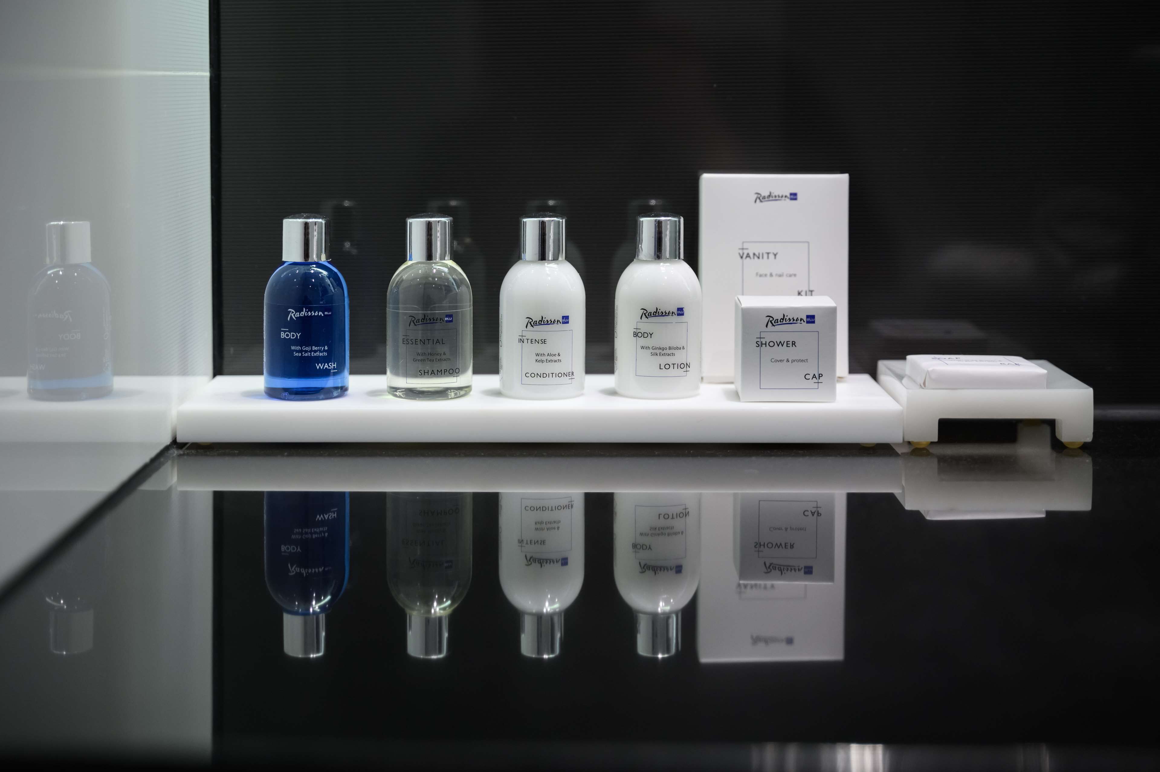 Presentación de varios productos de cuidado corporal Redissona, incluyendo gel de ducha, champú esencial, acondicionador intensivo, loción corporal, gorro de ducha y un neceser.