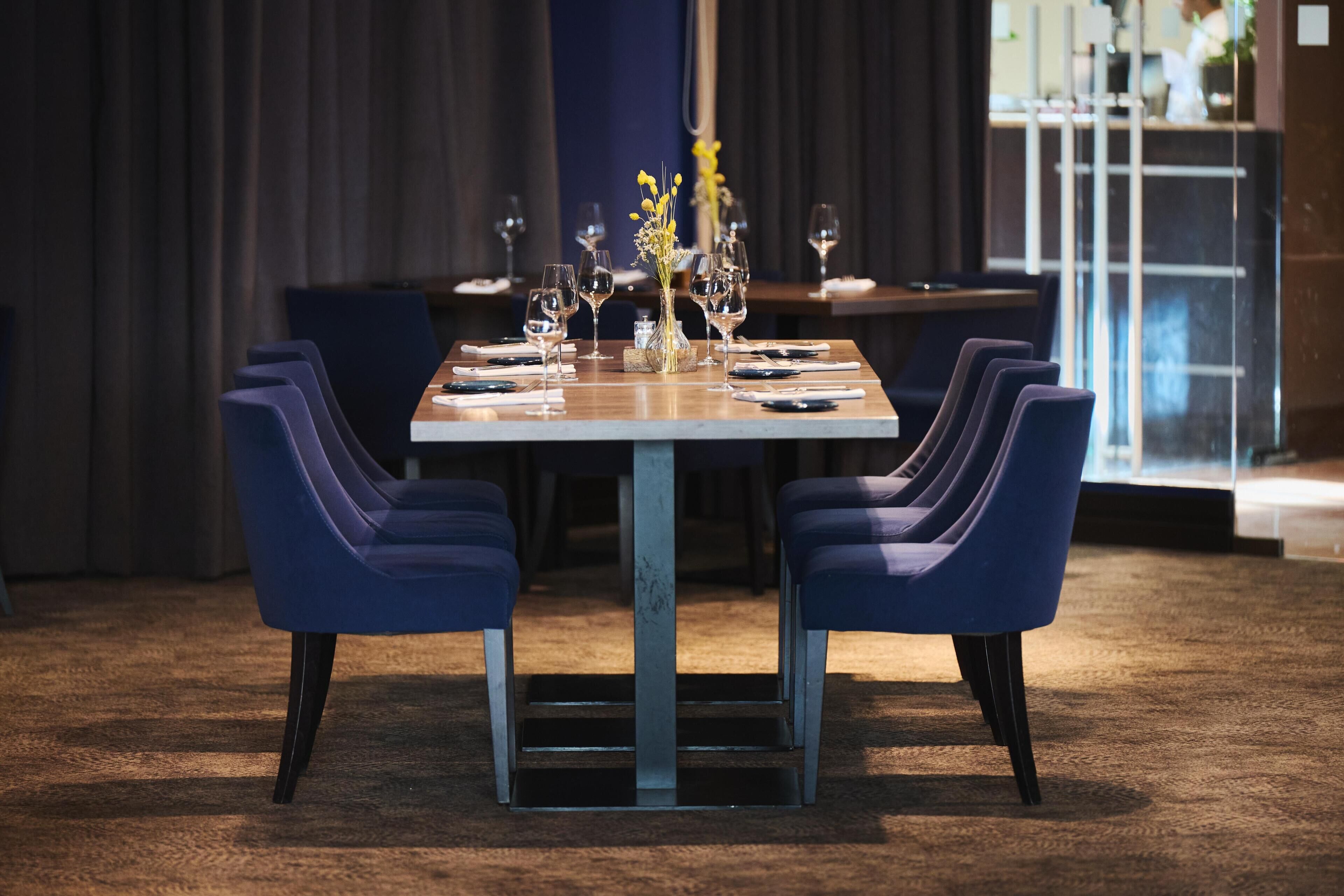 A dining table set with chairs, a vase with yellow flowers, and wine glasses.