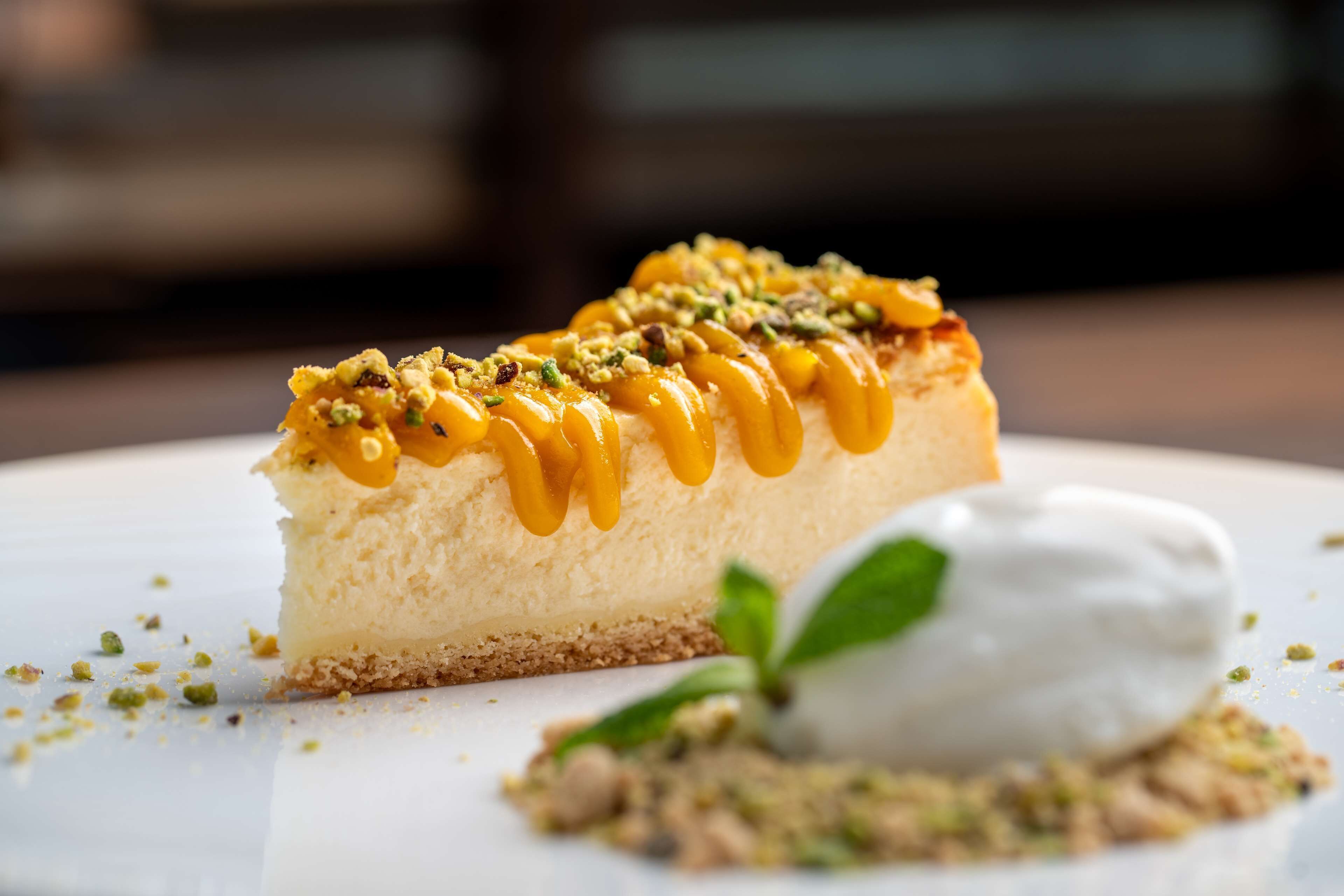 A slice of cheesecake with a drizzle of caramel and pistachio garnish on a white plate.