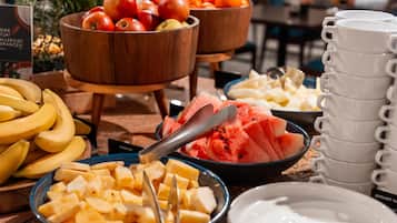 Un bufé con diversas frutas y una pila de tazas blancas.
