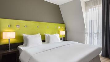 A hotel room with a large bed, two bedside tables with lamps, a green accent wall, and a view of the outdoors.