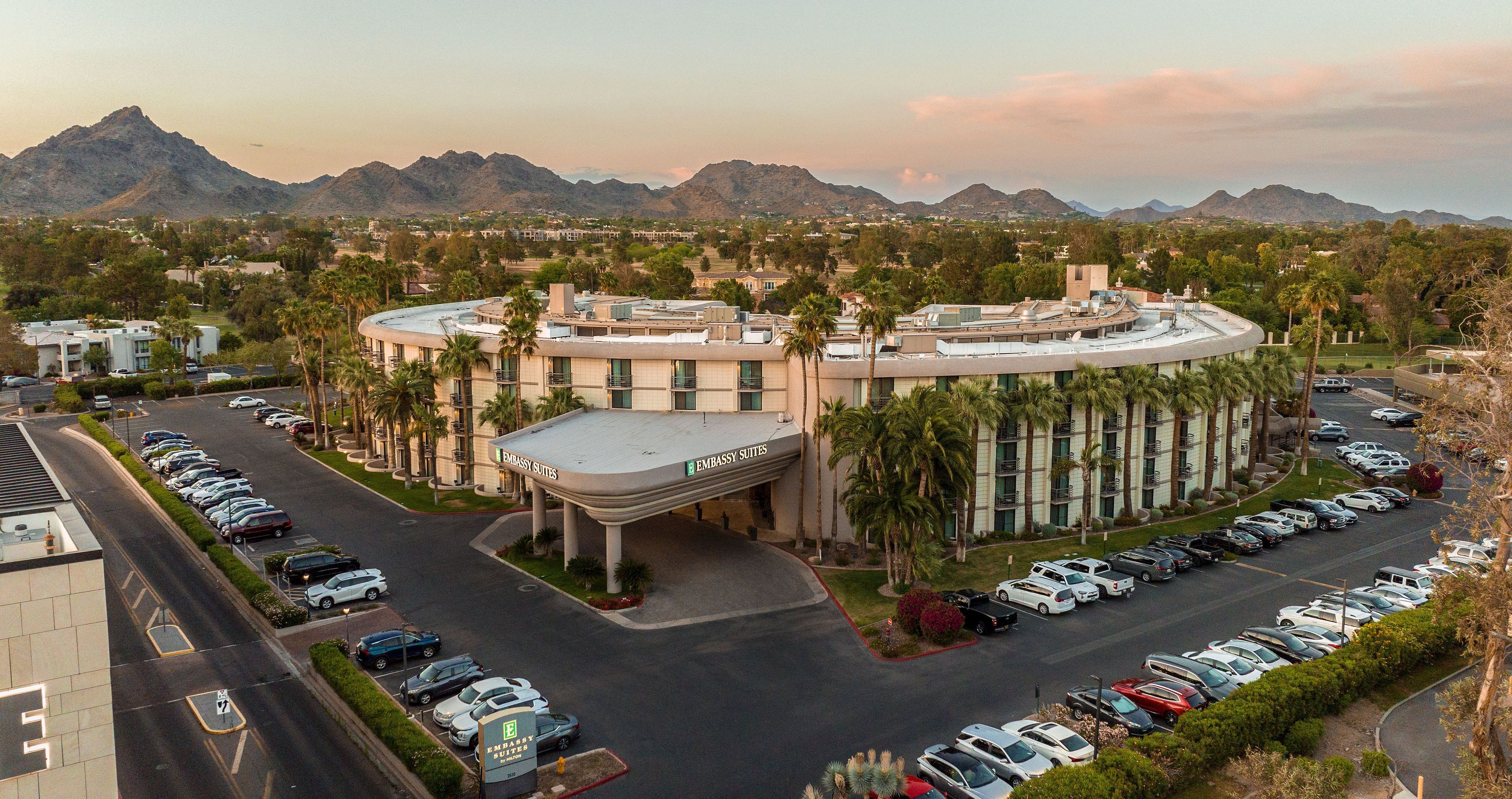 A hotel with a curved facade, a parking lot, and a mountainous backdrop.