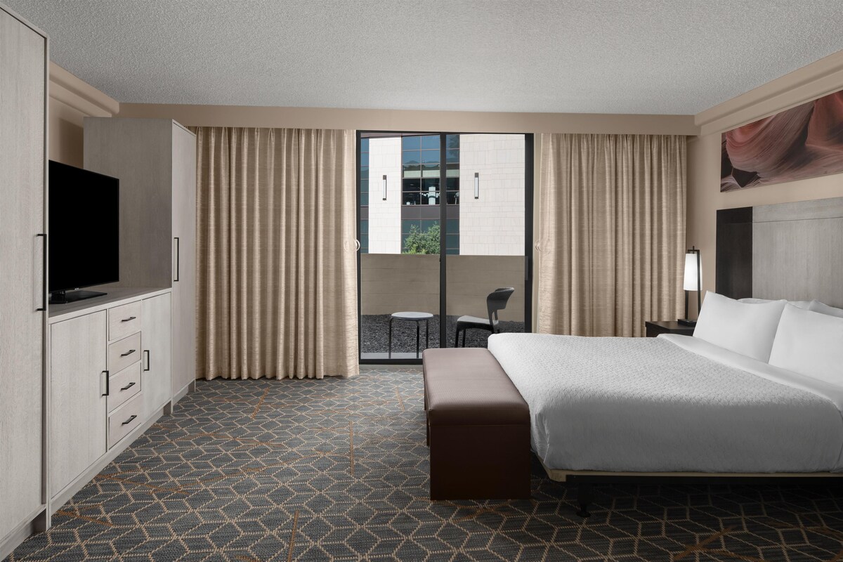 A hotel room with a bed, a TV, a desk, a chair, and a view of the outdoors.