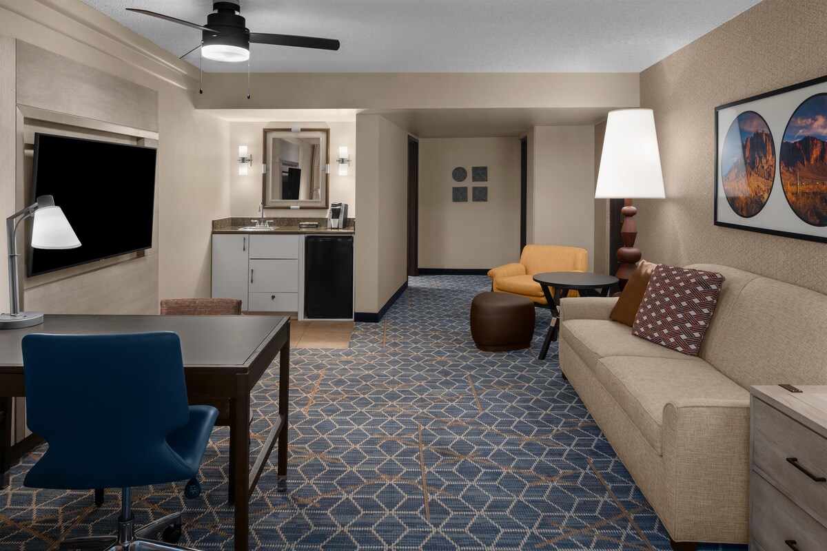 A hotel room with a dining area, kitchenette, and a seating area with a sofa and armchair.