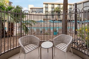 A balcony with two wicker chairs and a small table, overlooking a swimming pool and a building with balconies. - Embassy Suites by Hilton Phoenix Biltmore (Phoenix)