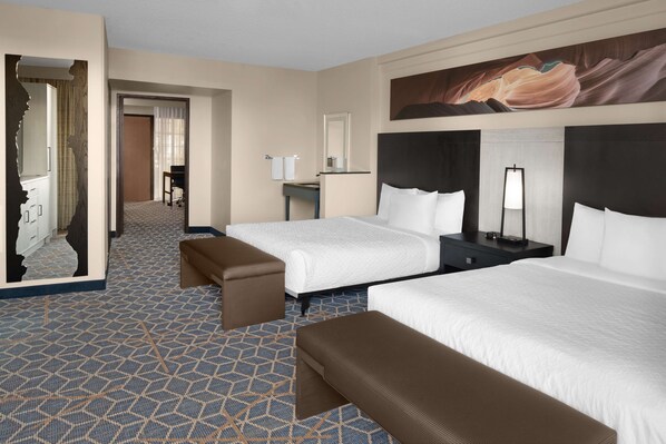 A hotel room with two beds, a desk, a chair, and a large painting on the wall.