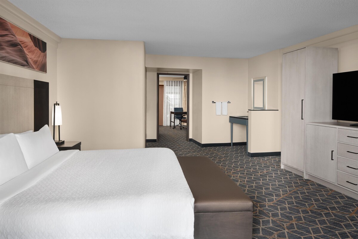 A hotel room with a large bed, a desk, a television, and a bathroom visible through an open door.