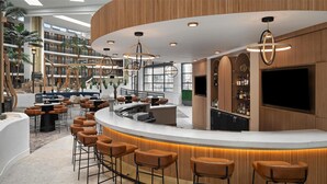 Un bar moderno con una barra curva, diversas opciones de asiento y una gran pantalla de televisión.