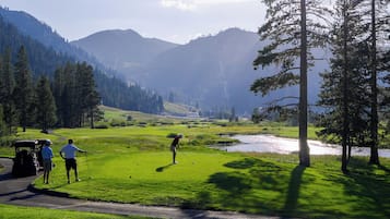 A golf course with a pond, trees, and mountains in the background.