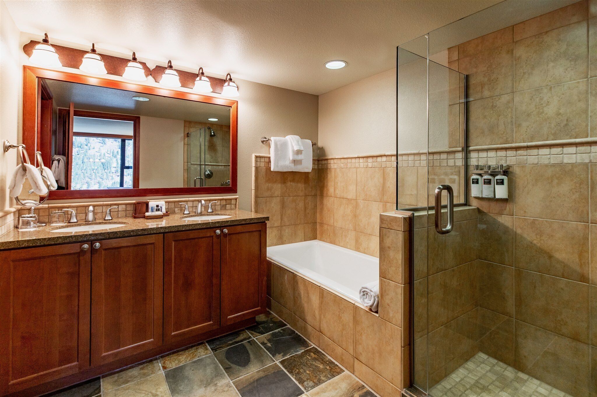 A bathroom with a wooden vanity, a large mirror, a bathtub, and a glass-enclosed shower.