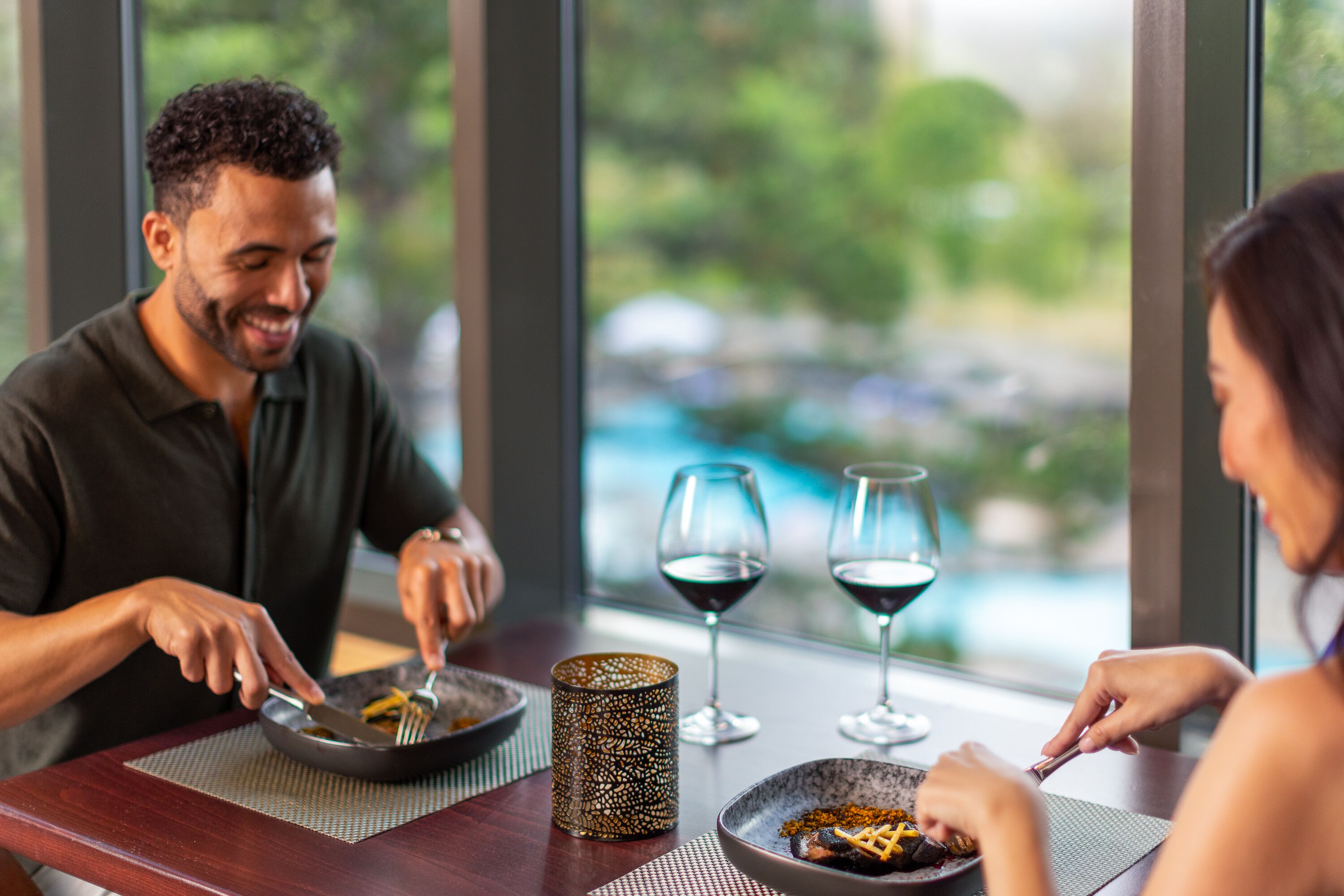 Mesa de jantar com duas pessoas comendo, dois copos de vinho e um castiçal decorativo.