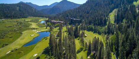 A golf course with a clubhouse, surrounded by dense forests and mountains.