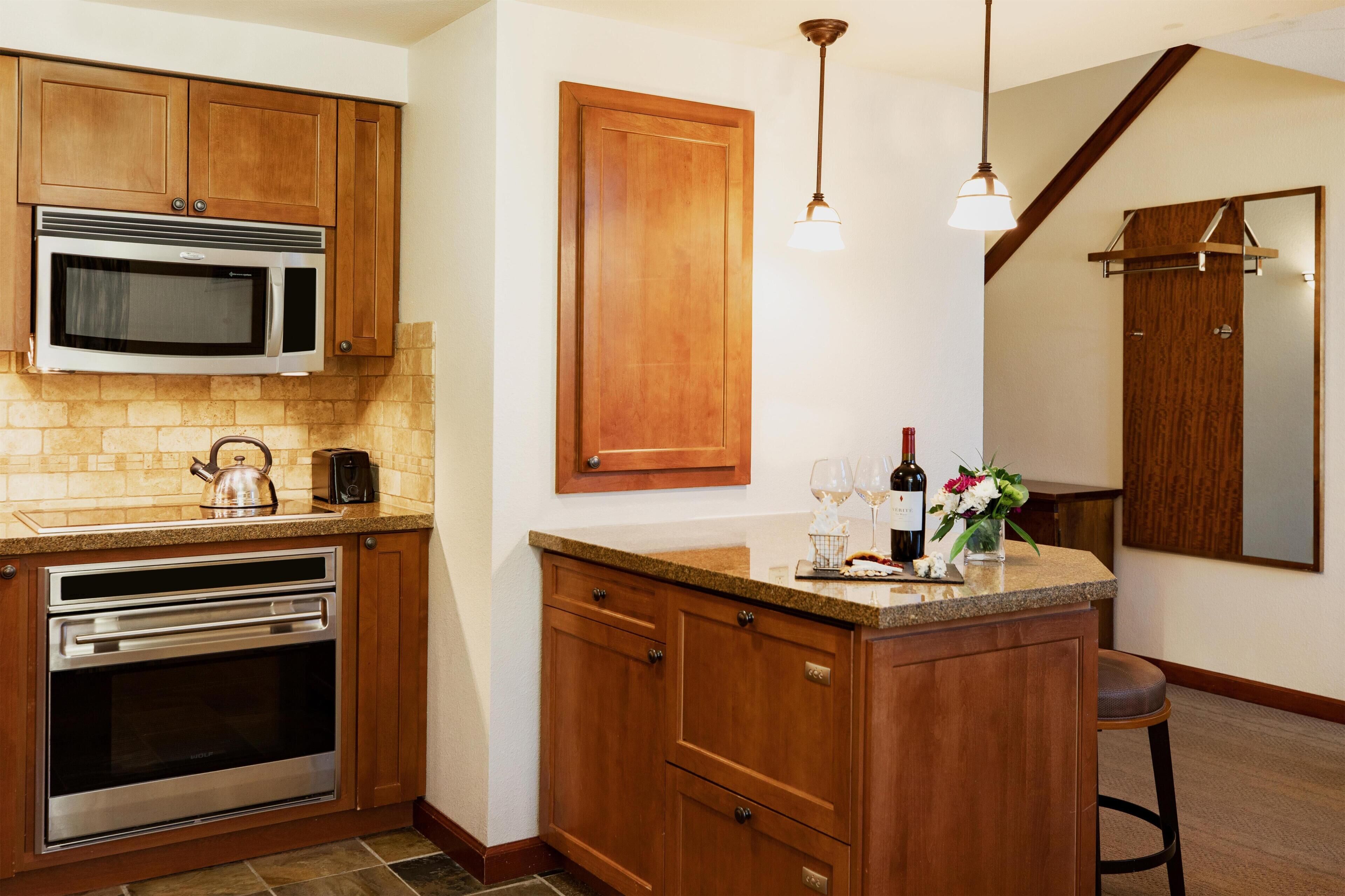 A kitchen with wooden cabinets, a built-in microwave, an oven, and a countertop with a kettle and wine glasses.