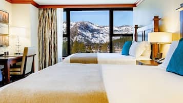 A hotel room with two beds, a TV, a desk, and a window with a mountain view.