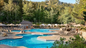 Ein Schwimmbecken mit Liegestühlen und Sonnenschirmen, umgeben von Bäumen und einem Bergpanorama.