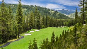 A golf course with sand bunkers, surrounded by dense forest and mountains.